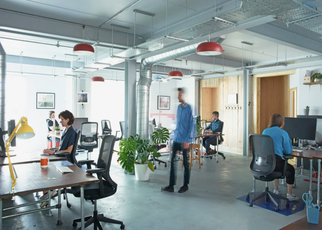 An open-plan coworking space featuring shared desks and people working in a bright style interior, highlighting a collaborative and welcoming work environment.